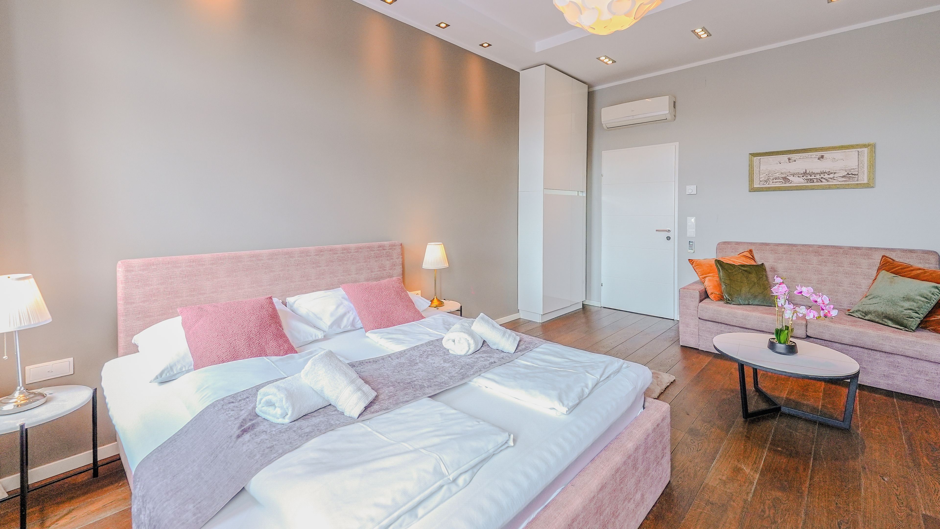 A modern hotel room with a large bed, a sofa, a small table, and a painting on the wall.