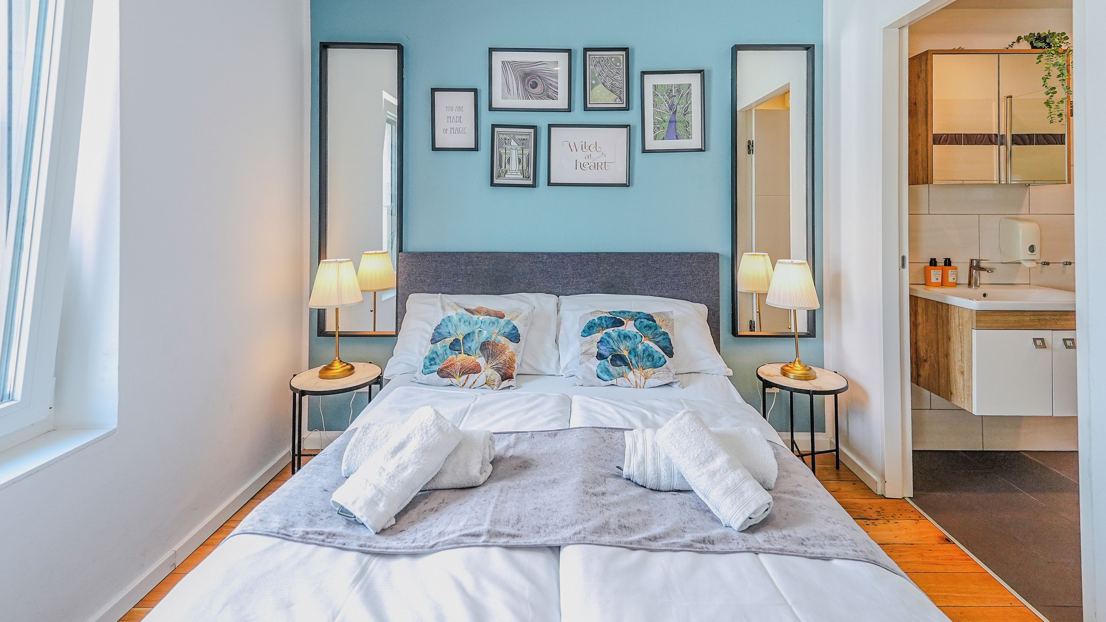 A hotel room with a bed, two bedside tables, a mirror, and a bathroom visible through an open door.