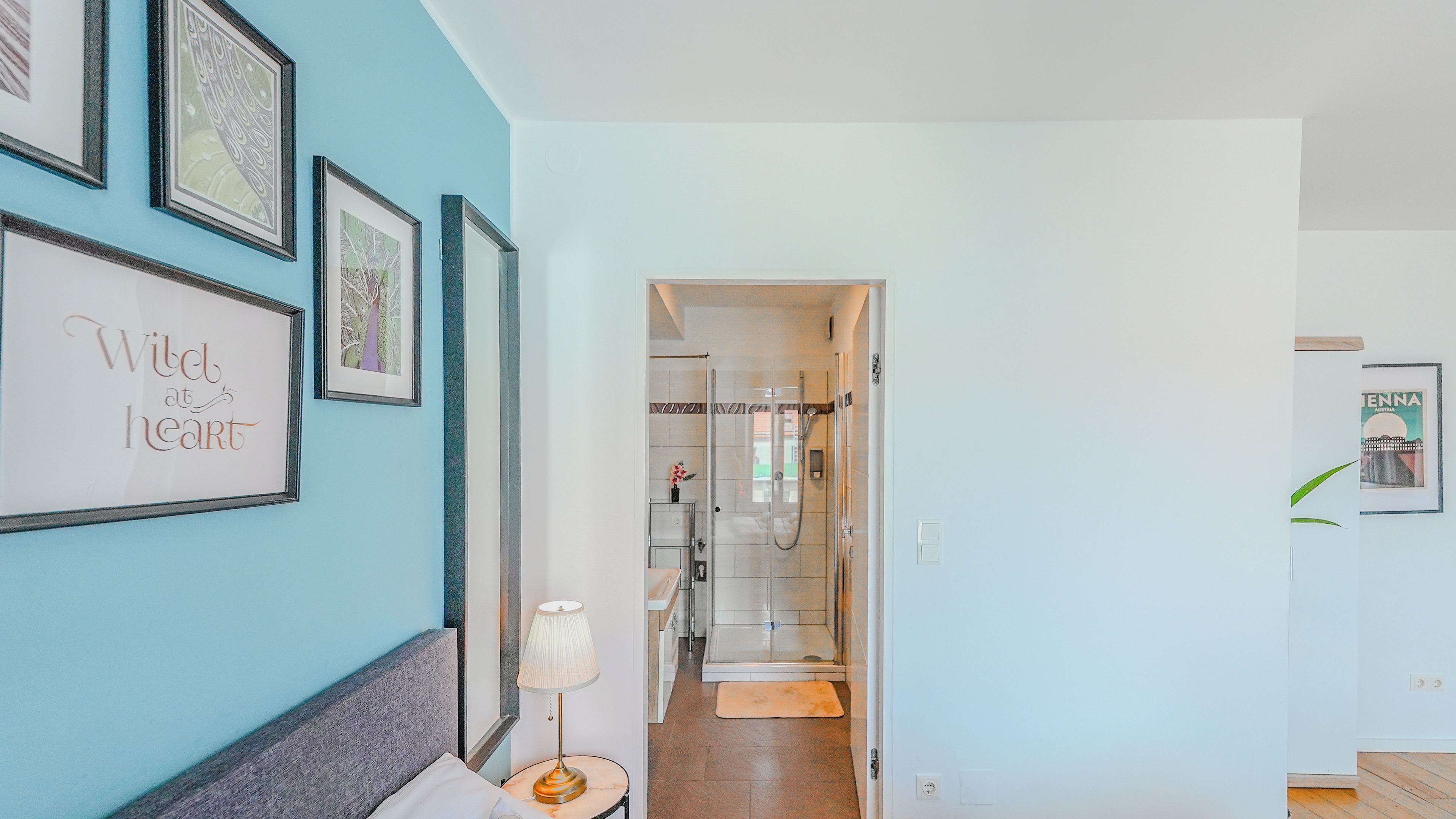 A hotel room with a bed, a nightstand, a lamp, and a wall with framed pictures.
