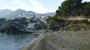 A coastal landscape with a rocky beach, a wooden fence, and buildings in the background.