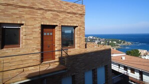 A modern building with a brick facade, a wooden door, and a balcony overlooking a coastal view.