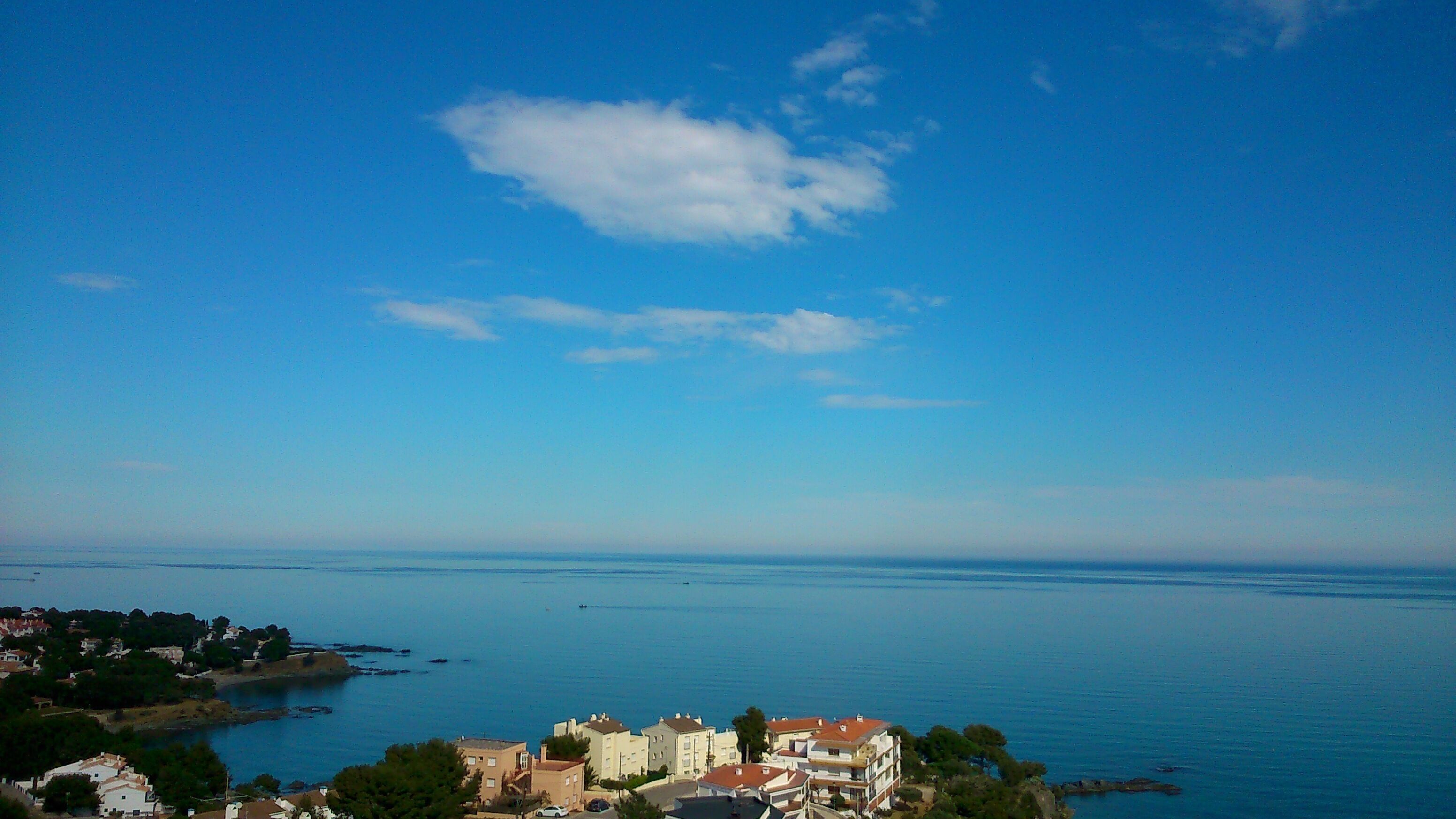 A coastal town with buildings along the shoreline, a clear blue sky, and calm sea.