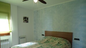 A bedroom with a bed, a nightstand, a ceiling fan, a radiator, and a window with curtains.