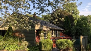 Une maison de plain-pied avec un porche à l’avant, entourée d’un jardin bien entretenu et d’arbres.