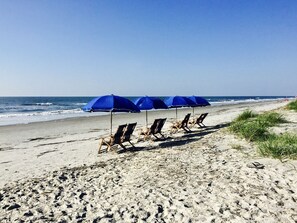 A beach with blue umbrellas and wooden chairs.