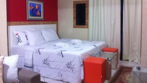 A hotel room with a bed, a small table, a chair, a red wall, and a window with curtains. - Pousada Requinte da Mantiqueira (Piracaia)