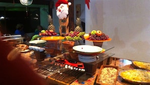 A buffet with various dishes, including fruits and a Santa Claus decoration. - Pousada Requinte da Mantiqueira (Piracaia)
