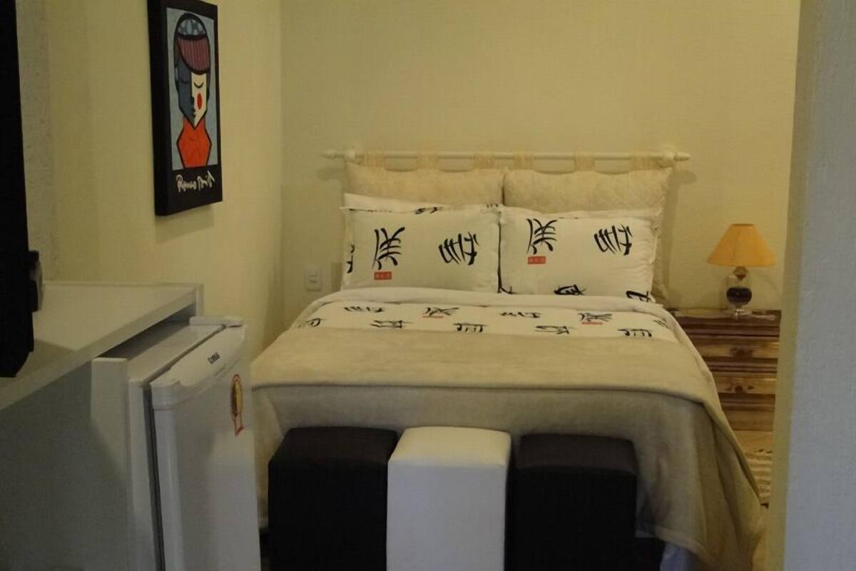 A bedroom with a bed, pillows with calligraphy, a bedside table with a lamp, and a small stool.
