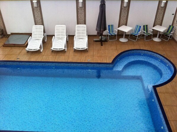 A swimming pool with lounge chairs and a small table. - Pousada Requinte da Mantiqueira (Piracaia)