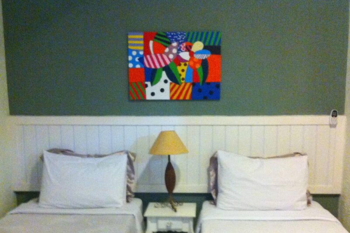 A hotel room with two beds, a nightstand, a lamp, and a colorful artwork on the wall.