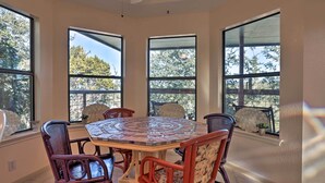 Un coin repas avec une table ronde et quatre chaises, de grandes fenêtres donnant sur la verdure et un ventilateur de plafond.