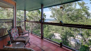 Un balcon abrité offrant une vue sur des arbres et une étendue d’eau. On y trouve deux chaises et une petite table sur laquelle est posé un vase.