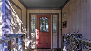 Une façade en bois avec une porte rouge, un perron dallé de pierres et un portail en métal.