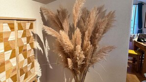 Ein Zimmer mit einem Holzkabinett mit geometrischen Mustern, einer Vase mit Pampasgras und einem Holzboden.