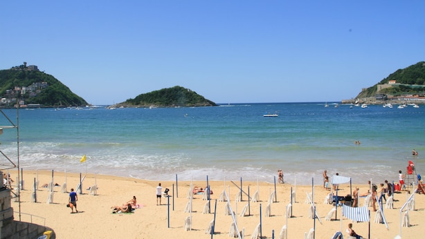 Ein Strand mit Sonnenschirmen, Menschen und blauem Himmel.