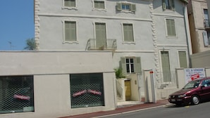 Ein zweistöckiges Gebäude mit weißer Fassade, zahlreichen Fenstern mit Fensterläden und einem sichtbaren Schaufenster mit einem Schild.