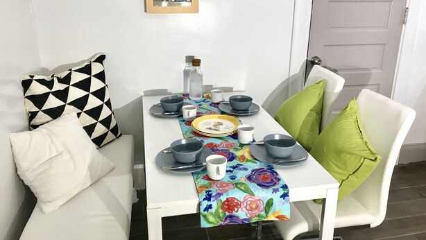 A dining area with a table set for two, featuring a floral table runner, two chairs with cushions, and a framed picture on the wall. - Upscale 1BR Loft near UC, DAAP, CCM, Hospital and Zoo w/Parking, 3FL (Cincinnati)