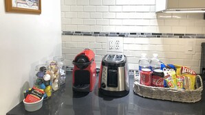 A kitchen with white tiled backsplash, a toaster, a coffee maker, a jar of cookies, a basket of snacks, and a framed picture on the wall. - Upscale 1BR Loft near UC, DAAP, CCM, Hospital and Zoo w/Parking, 3FL (Cincinnati)