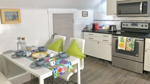 A compact kitchen with white cabinets, a microwave, a stove, and a dining table set with bowls, plates, and a colorful placemat. - Upscale 1BR Loft near UC, DAAP, CCM, Hospital and Zoo w/Parking, 3FL (Cincinnati)