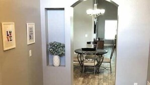 A hallway with a wooden floor, a dining area with a table and chairs, and framed pictures on the walls.