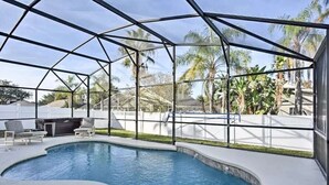 An indoor swimming pool with a glass enclosure, surrounded by palm trees and a patio area with chairs.