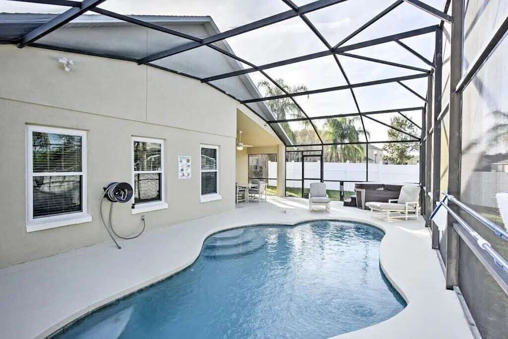 An indoor swimming pool with a glass ceiling, surrounded by a covered patio area with seating.