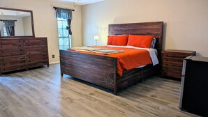 Een slaapkamer met een houten bed, een dressoir, een nachtkastje en een spiegel.