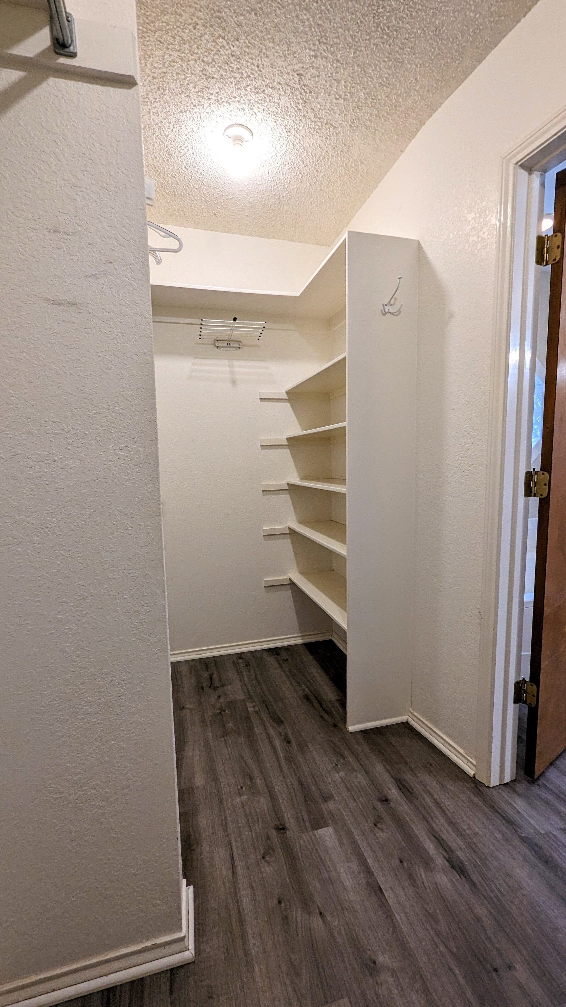 Un vestidor con estanterías blancas y suelo de madera.