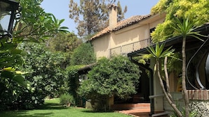 Un jardín cuidado con diversas plantas y un camino que conduce a un edificio con techo de tejas y un balcón.