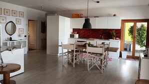 Una cocina moderna con armarios blancos, un salpicadero de ladrillo rojo y un comedor con mesa y sillas de madera.