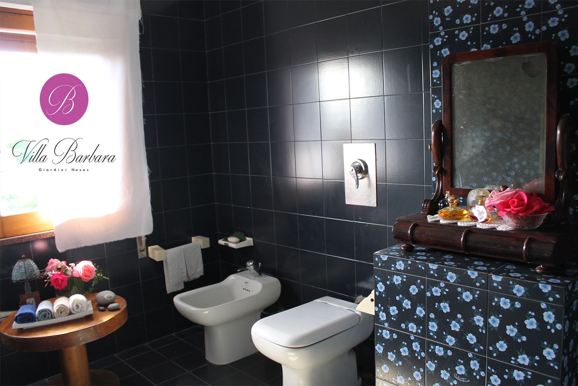 A bathroom with black tiles, a bidet, a toilet, and a vanity with a mirror.