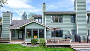 A two-story house with a covered porch, a grill, and a fenced deck area. - Mountain Harbor Vibrant Vista at Whitefish Lake (Whitefish)