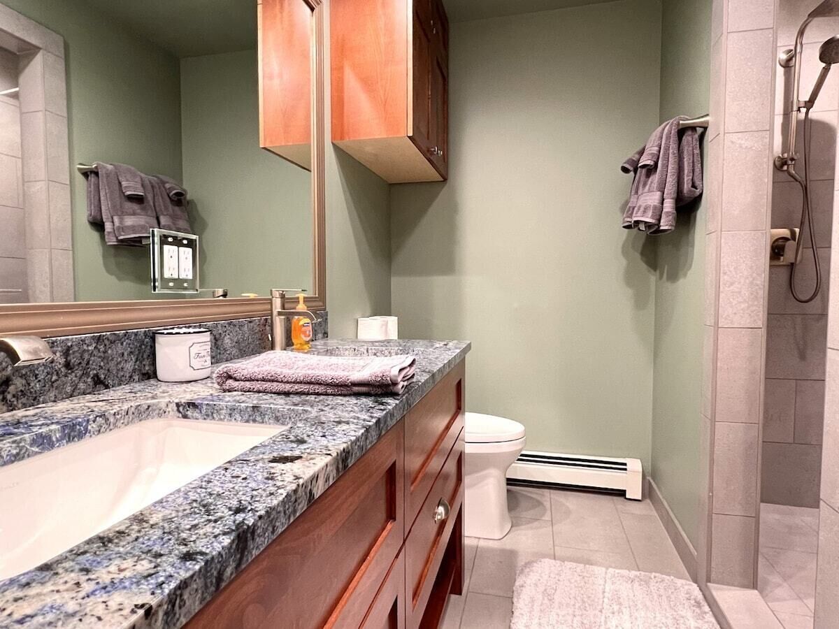 A bathroom with a granite countertop, a white toilet, a towel rack, and a shower area.