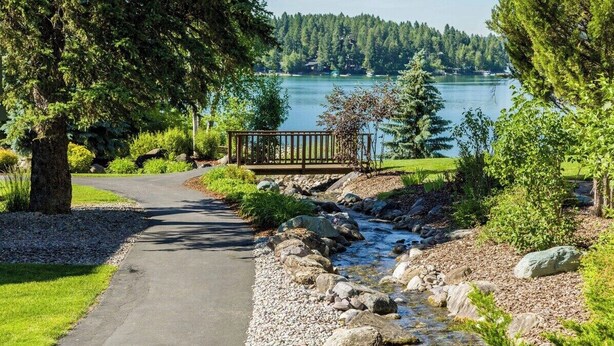 A pathway leading to a wooden deck overlooking a lake, surrounded by trees and pebbles. - Mountain Harbor Vibrant Vista at Whitefish Lake (Whitefish)