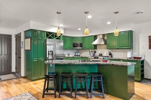 Uma cozinha moderna com armários verdes, uma geladeira de aço inoxidável, micro-ondas e uma ilha grande com banquetas.