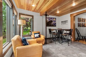 Interior moderno com teto de madeira, área de refeições com cadeiras de metal e uma grande janela com vista para um jardim.
