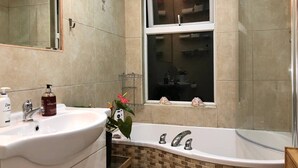 A bathroom with a white sink, a mirror, a window, and a bathtub with a mosaic tile surround. - Double bedroom near Heathrow (Hayes)