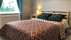 A bedroom with a patterned bedspread, a wooden headboard, a bedside lamp, and a window with curtains. - Double bedroom near Heathrow (Hayes)