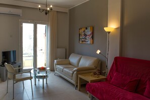 A living room with a beige sofa, a red sofa, a glass coffee table, a white armchair, and a TV.
