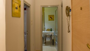 Een gang die uitkomt in een eetruimte met een tafel en stoelen, een telefoon aan de muur en een deur aan de rechterkant.