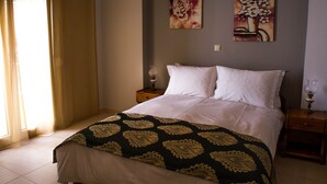 Een slaapkamer met een bed, twee nachtkastjes, een raam met gordijnen en twee bloemrijke schilderijen aan de muur.