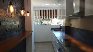 A modern kitchen with a stone wall, pendant lights, a window with a view, and stainless steel appliances. - seafront apartment with panoramic view to the ocean (El Campello, Alicante)