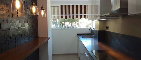 A modern kitchen with a stone wall, pendant lights, a window with a view, and stainless steel appliances.