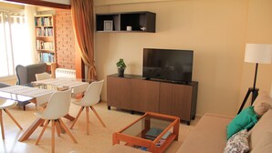 A living room with a sofa, a coffee table, a TV, a bookshelf, and a dining area with chairs and a table. - seafront apartment with panoramic view to the ocean (El Campello, Alicante)