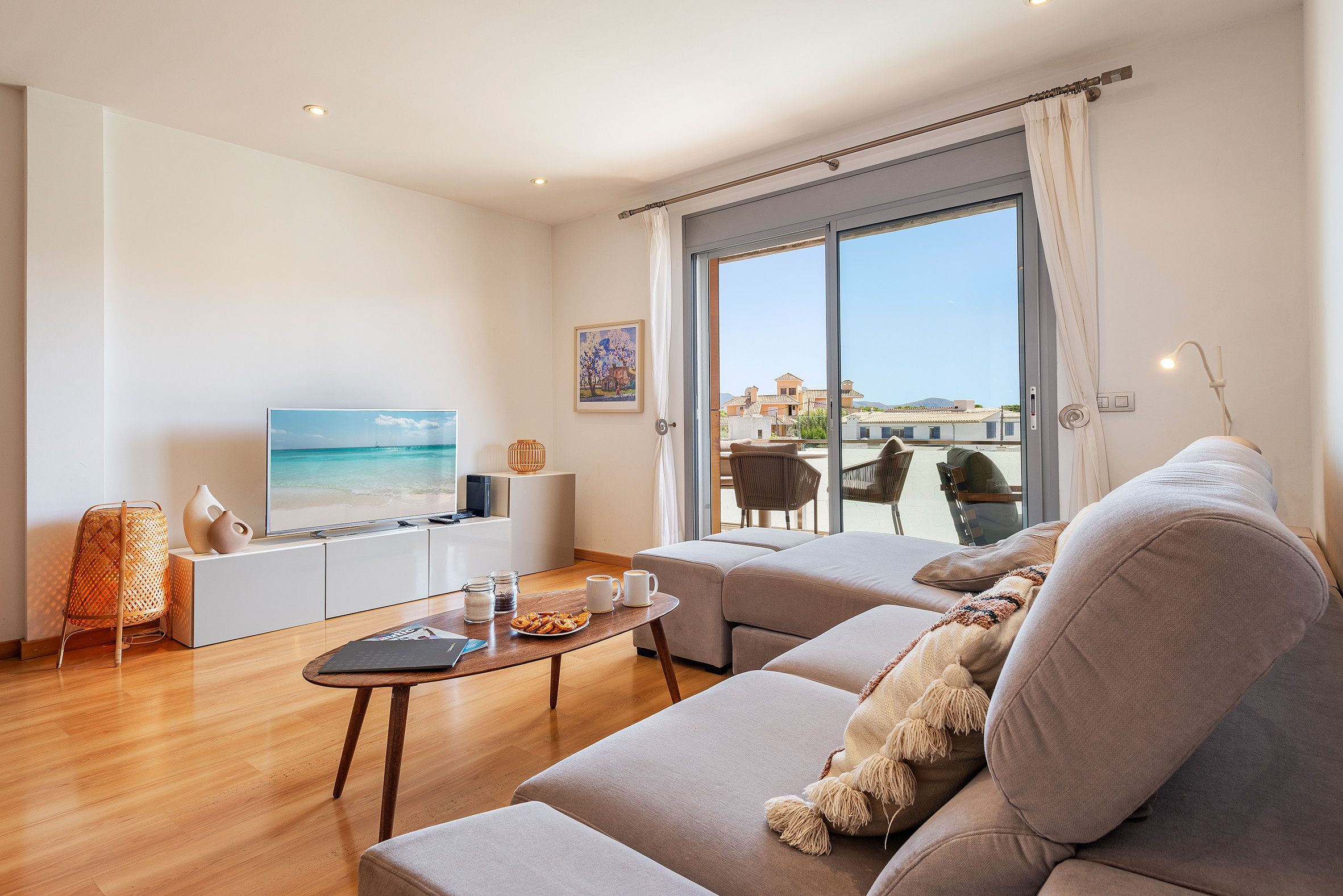 Una sala de estar moderna con una televisión de pantalla plana, un sofá, una mesa de centro y vistas al mar a través de amplios ventanales.
