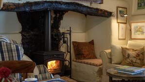 A cozy living room with a stone fireplace, a sofa, a chair, and a table with a book and a plate of food. - Thatched Irish Cottage in Beautiful and Tranquil Countryside (Limerick)