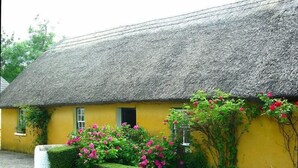 A yellow building with a thatched roof, surrounded by well-maintained hedges and flowering plants. - Thatched Irish Cottage in Beautiful and Tranquil Countryside (Limerick)