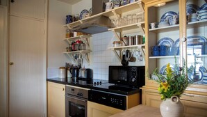 A kitchen with a stove, microwave, oven, and various kitchen utensils on shelves. - Thatched Irish Cottage in Beautiful and Tranquil Countryside (Limerick)
