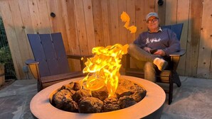 Une personne est assise près d’un foyer en pierre où brûle un feu.