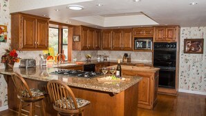 Eine Küche mit Holdelementen, Granit Arbeitsplatten, einer zentralen Kochinsel mit Barhocker, einer Mikrowelle, einem Backofen und einem Spülbecken.